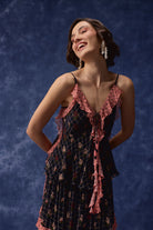 A woman wearing a dark navy and pink floral slip dress with ruffled trim, posing against a textured dark blue backdrop.
